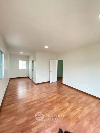 Spacious empty room with wooden flooring and white walls, ideal for customization.