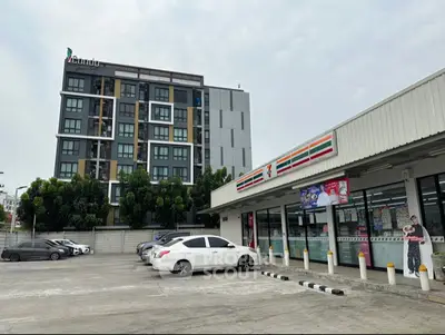 Modern condo building next to a convenience store with ample parking space.