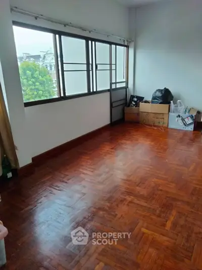 Spacious empty room with wooden flooring and large windows offering natural light.