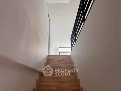 Modern staircase with wooden steps and sleek black railing in a bright interior space.