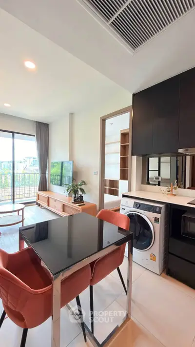 Modern open-plan living room with sleek kitchen and washer, featuring a balcony view.