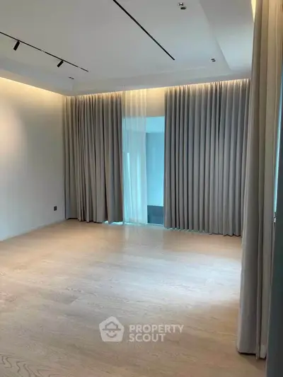 Spacious empty room with elegant floor-to-ceiling curtains and wooden flooring