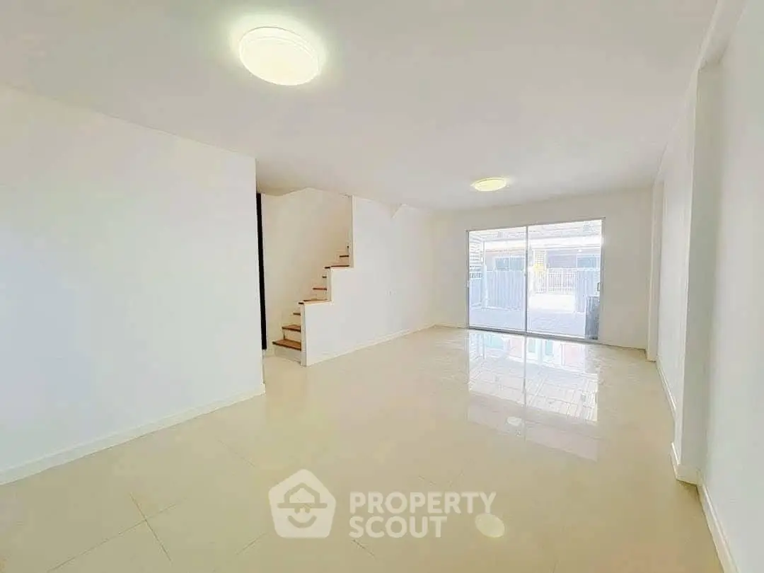 Spacious open-plan living room with modern staircase and large windows.