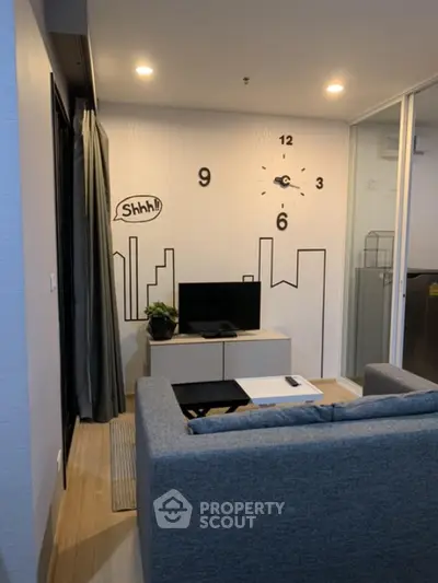 Modern living room with stylish wall clock and cityscape decor, featuring a cozy gray sofa and sleek TV setup.
