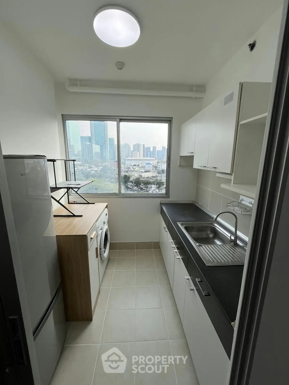 Modern kitchen with city view, featuring sleek cabinets, washing machine, and fridge in a compact layout.