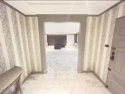Elegant entryway leading to a spacious living room with marble flooring and stylish wallpaper.