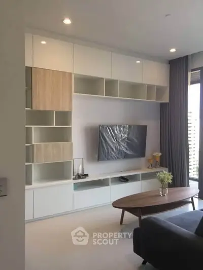 Modern living room with sleek cabinetry and large TV, featuring a stylish coffee table and elegant decor.