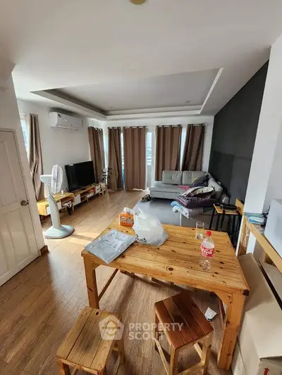 Spacious living room with modern decor and natural light, featuring wooden furniture and a cozy ambiance.