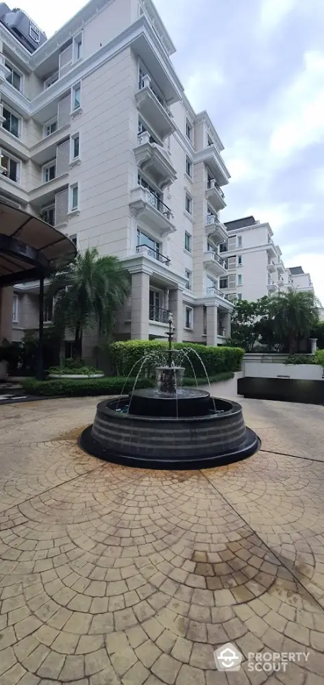 Elegant residential building with fountain and lush greenery in a serene setting.