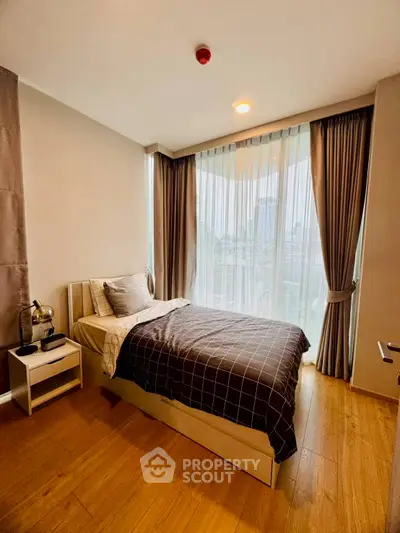 Cozy bedroom with large windows and city view, featuring modern decor and wooden flooring.