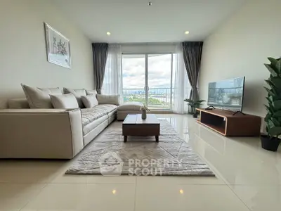 Modern living room with large sofa, TV, and balcony view.