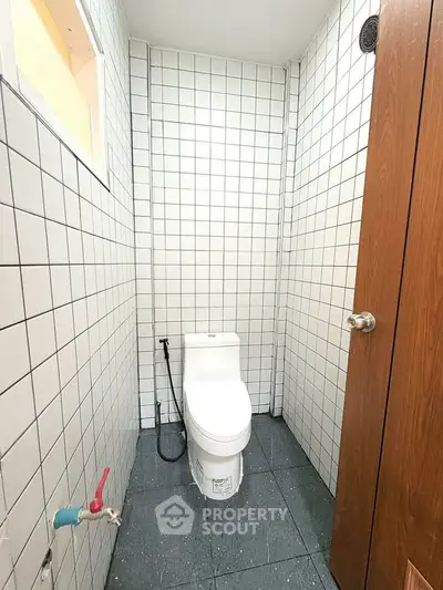 Compact tiled bathroom with modern toilet and wooden door, ideal for small spaces.