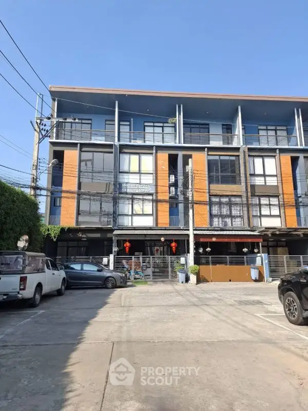 Modern multi-story building with parking area and vibrant facade under clear blue sky.
