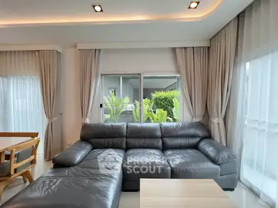 Spacious modern living room with large leather sectional sofa and natural light from large windows.