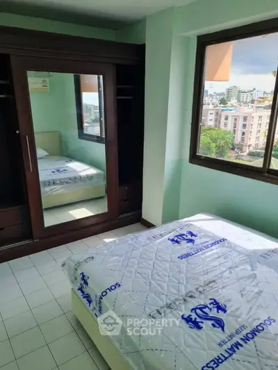 Cozy bedroom with large mirrored wardrobe and city view from window.