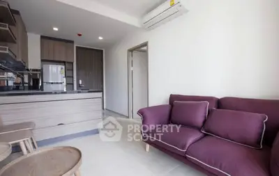 Modern living room with stylish purple sofa and sleek kitchen area in open layout apartment.