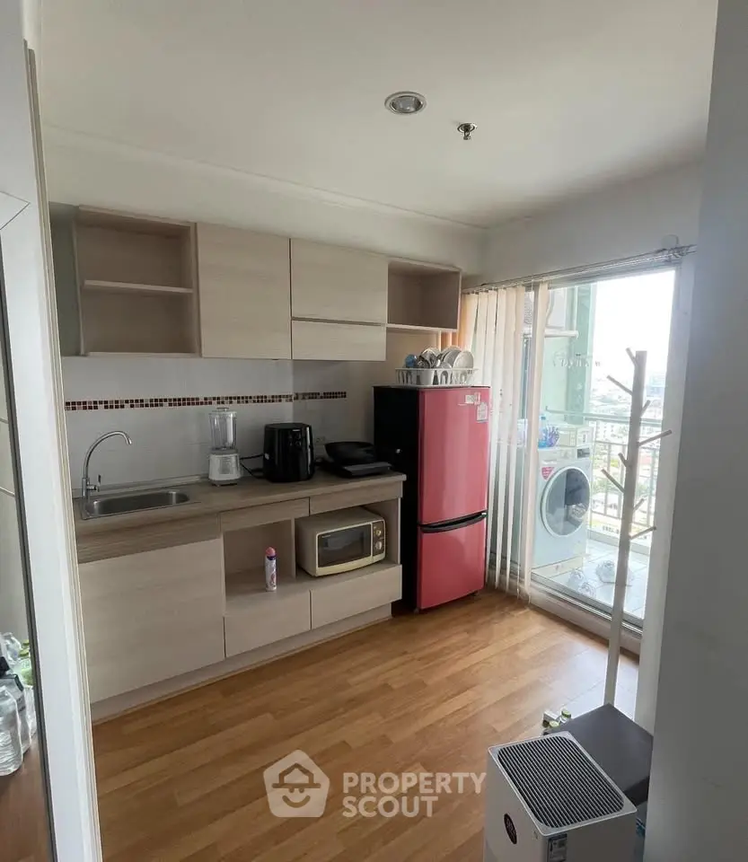 Modern kitchen with red fridge and balcony view, featuring wooden flooring and ample storage.