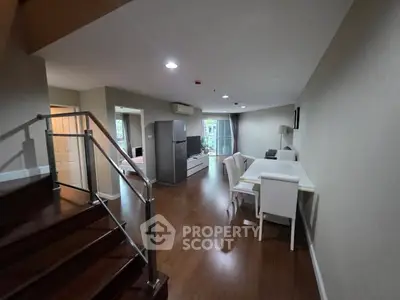 Spacious modern living room with dining area and staircase, featuring sleek wooden flooring.