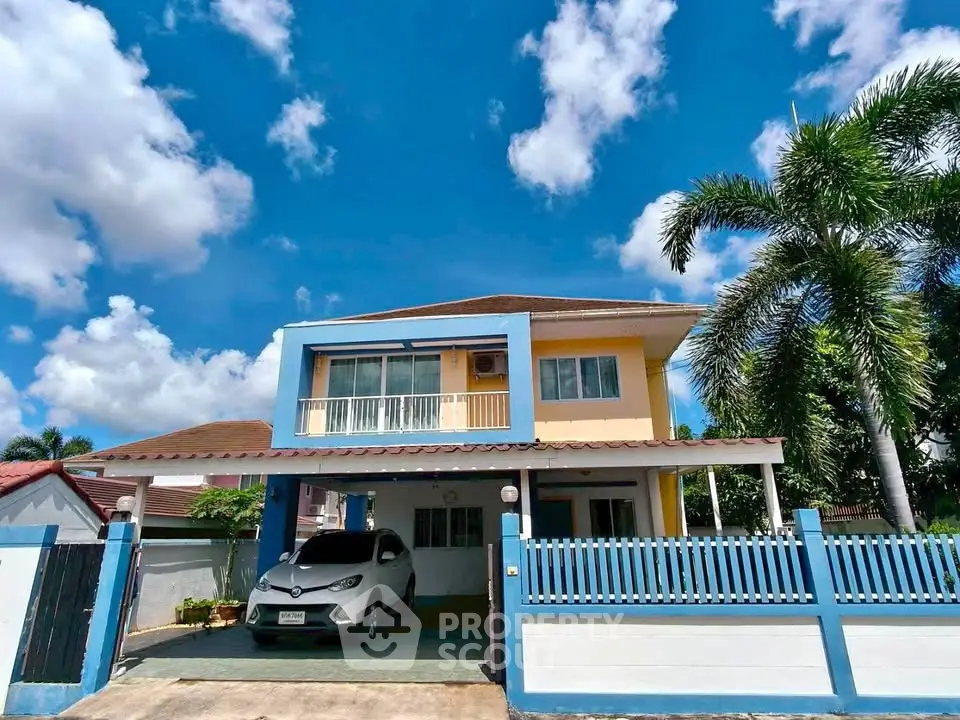 Charming two-story house with driveway and lush palm trees under a clear blue sky.