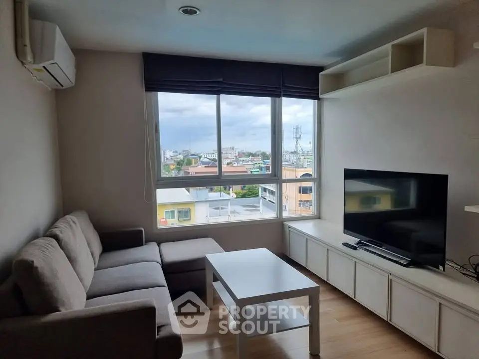 Modern living room with large window and city view, featuring a cozy sofa and flat-screen TV.