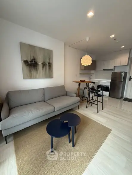 Modern living room with stylish decor and open kitchen layout, featuring a cozy gray sofa and contemporary lighting.