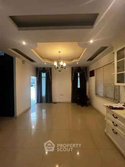 Spacious living room with elegant ceiling design, ambient lighting, and glossy tiled flooring, featuring large windows with classic drapery.