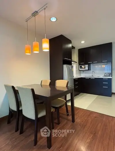 Modern kitchen with dining area featuring sleek dark cabinets and stylish lighting.