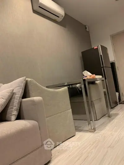 Modern living room with sleek furniture and air conditioning, featuring a compact dining area and refrigerator.