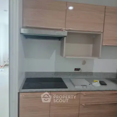 Modern kitchen with sleek wooden cabinets and electric cooktop in a stylish apartment.