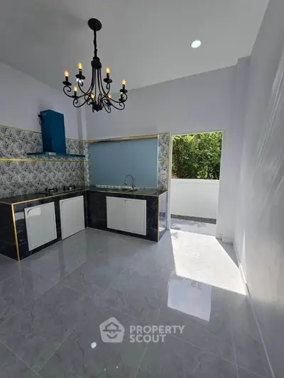 Modern kitchen with elegant chandelier and open layout, featuring sleek cabinetry and natural light.