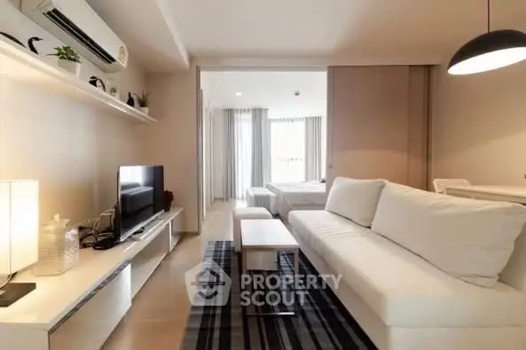 Modern living room with cozy sofa and sleek TV setup, leading to a bright bedroom.
