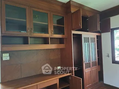 Spacious wooden storage unit with glass cabinets and built-in desk in a well-lit room.