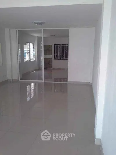 Spacious empty room with glossy tiled floors and large glass partition, ideal for customization.