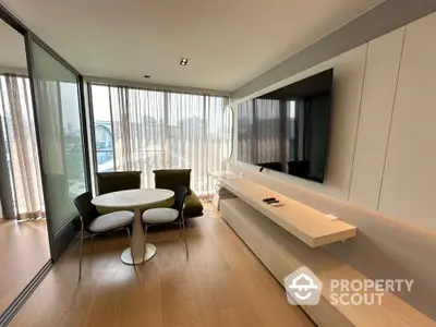 Modern living room with sleek furniture and large TV, featuring floor-to-ceiling windows and wooden flooring.