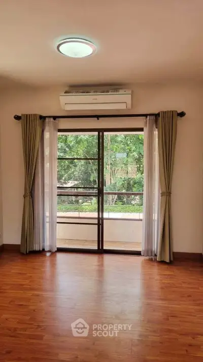 Spacious room with wooden flooring and large window overlooking greenery, perfect for natural light lovers.