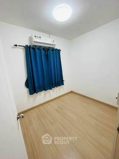 Minimalist bedroom with wooden flooring and blue curtains, featuring air conditioning for comfort.