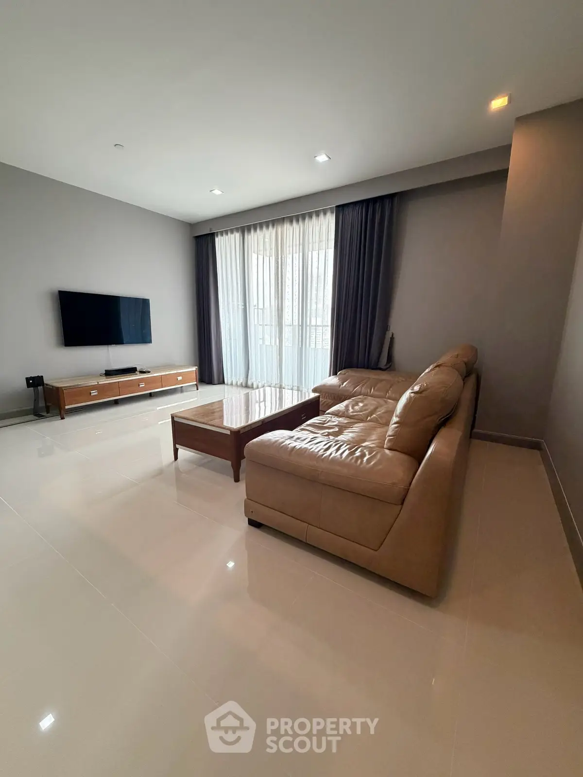 Spacious modern living room with sleek leather sofa and wall-mounted TV, perfect for relaxation.