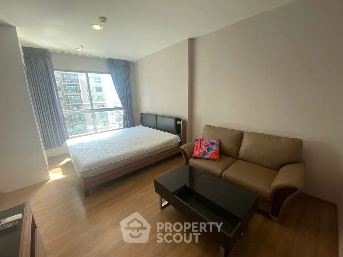 Bright studio apartment with bed and sofa, large window view, and wooden flooring.