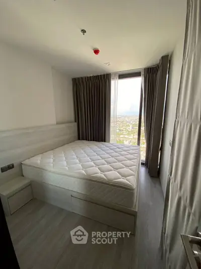 Modern bedroom with large window offering stunning city view, featuring a comfortable bed and elegant curtains.