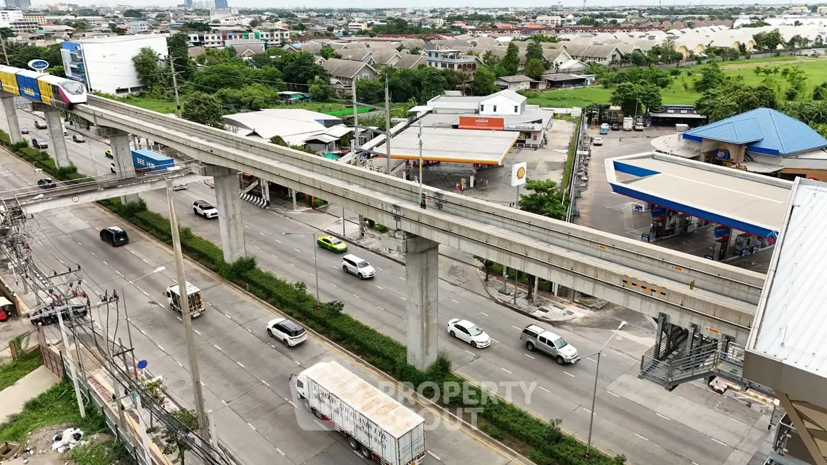 Aerial view of urban road with elevated train tracks and nearby gas stations.