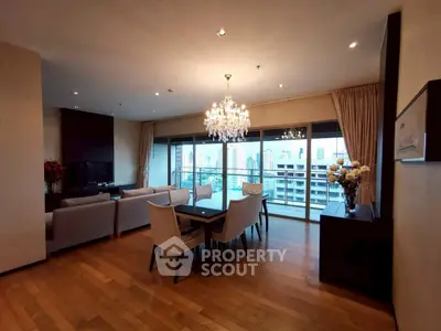 Elegant living room with chandelier and city view, featuring modern furniture and wooden flooring.