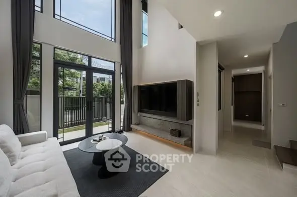 Spacious modern living room with high ceilings and large windows offering natural light and garden view.