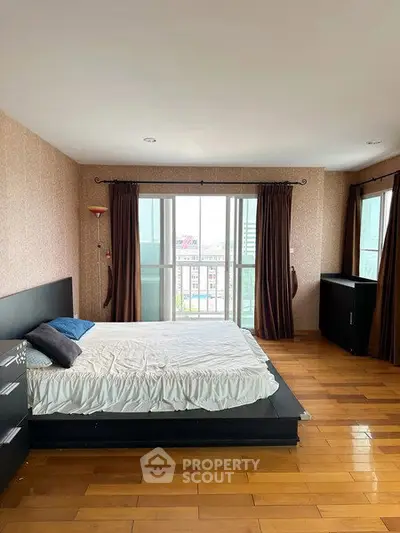 Spacious bedroom with wooden flooring and large windows offering city views.