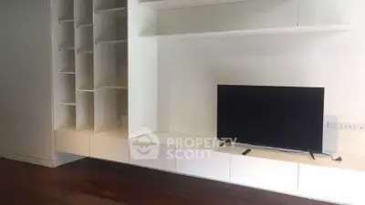 Modern living room with sleek built-in shelving and flat-screen TV on wooden floor.