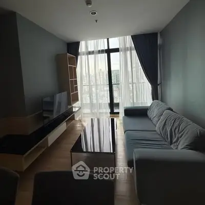 Modern living room with large windows and city view, featuring a sleek sofa and entertainment unit.