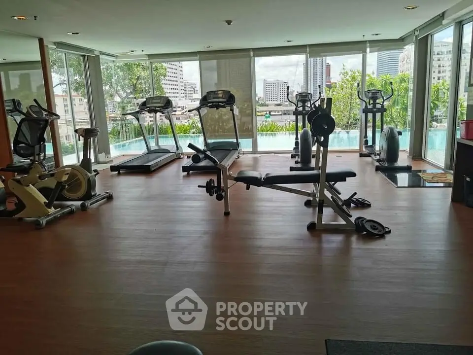 Spacious gym with modern equipment and city view, perfect for fitness enthusiasts.