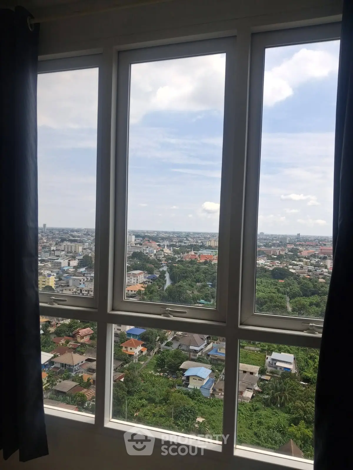 Stunning high-rise view from a window overlooking a vibrant cityscape and lush greenery.