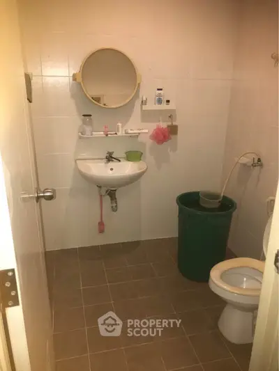 Compact bathroom with basic fixtures and tiled walls, featuring a round mirror and a small sink.