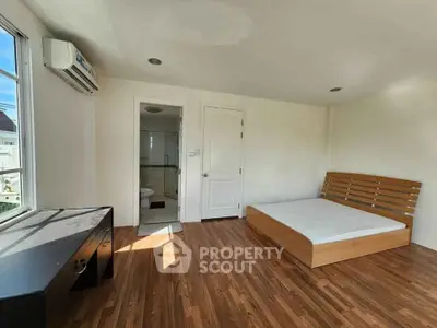 Spacious bedroom with wooden flooring, large window, and modern furniture in a bright apartment.