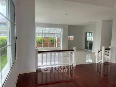 Spacious modern living room with polished wooden floors and large windows offering garden views.